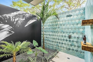 Un bany modern amb paret arrebossada, una palmera i una zona de dutxa.
