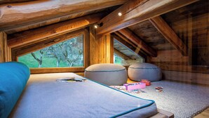 A cozy attic bedroom with a bed, two bean bags, and a window overlooking a green landscape.