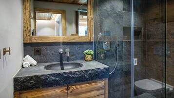 Un bagno moderno con un piano di lavoro in granito, mobili in legno, un ampio specchio e una cabina doccia con pareti in vetro.