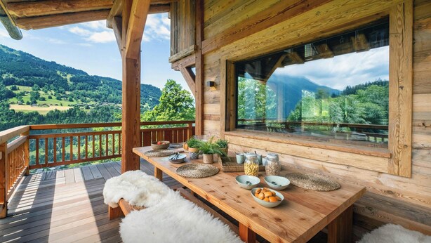 A wooden deck with a table set for dining, overlooking a mountainous landscape.