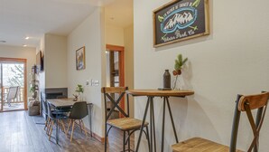 A dining area with a wooden table and chairs, a wall-mounted sign, and a view into another room. - Winter Park Condo w/ Balcony & Mtn Views! (Winter Park)