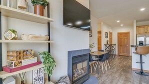 A modern living room with a fireplace, a flat-screen TV mounted on the wall, and a dining area with wooden furniture. - Winter Park Condo w/ Balcony & Mtn Views! (Winter Park)