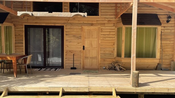 A wooden cabin with a large sliding glass door, a dining table with chairs, and a small porch area. - Cabañas Mi Refugio Puerto Varas (Puerto Varas)