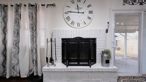 A living room with a white brick fireplace, a large wall clock, and a "Welcome To" sign above the door. - Cozy Parkview Oasis With Gameroom (Amarillo)