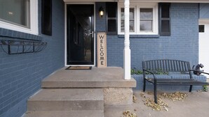 A blue house with a 'WELCOME' sign, a bench, and a doormat. - Cozy Parkview Oasis With Gameroom (Amarillo)