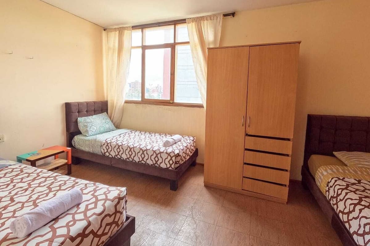 A bedroom with a bed, a wardrobe, a window with curtains, and a small table.
