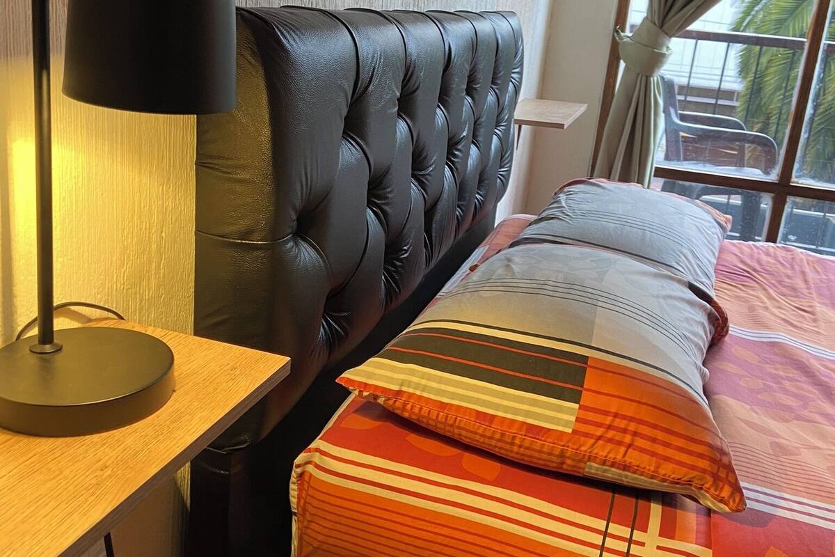 A bedroom with a tufted headboard, a bedside table with a lamp, and a window with curtains.