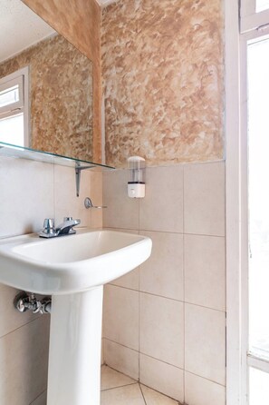 Une salle de bain avec un lavabo blanc, une étagère en verre et un miroir.