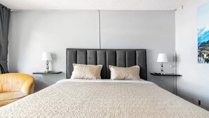 A modern hotel room with a large bed, two bedside lamps, a chair, and a cityscape painting on the wall. - Blue house la floresta (Quito)
