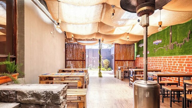 A restaurant with wooden tables and benches, a stone wall, and a brick wall with a green mural. - Blue house la floresta (Quito)