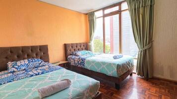 Una habitación con dos camas, piso de madera y una ventana con cortinas.