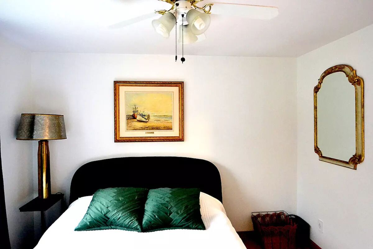 Una camera d'albergo con un letto, una ventola a soffitto, un quadro appeso al muro e uno specchio.