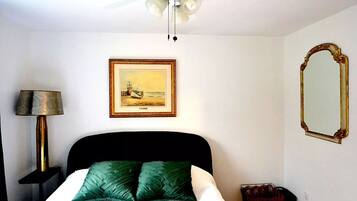 Una camera d'albergo con un letto, una ventola a soffitto, un quadro appeso al muro e uno specchio.