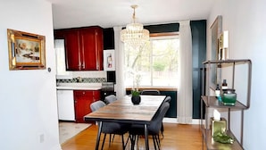 A modern kitchen with red cabinets, a dining table with chairs, a chandelier, and a window with curtains. - Cellar House NOTL - Entire Home in the Heart of Niagara-on-the-Lake (Niagara-on-the-Lake)