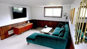 A living room with a teal sofa, a wooden coffee table, a TV mounted on the wall, and a window with blinds. - Cellar House NOTL - Entire Home in the Heart of Niagara-on-the-Lake (Niagara-on-the-Lake)