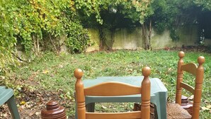 A patio area with a wooden table and chairs, surrounded by greenery and a tiled floor. - Auberge Rose - Hostel (Noisiel)
