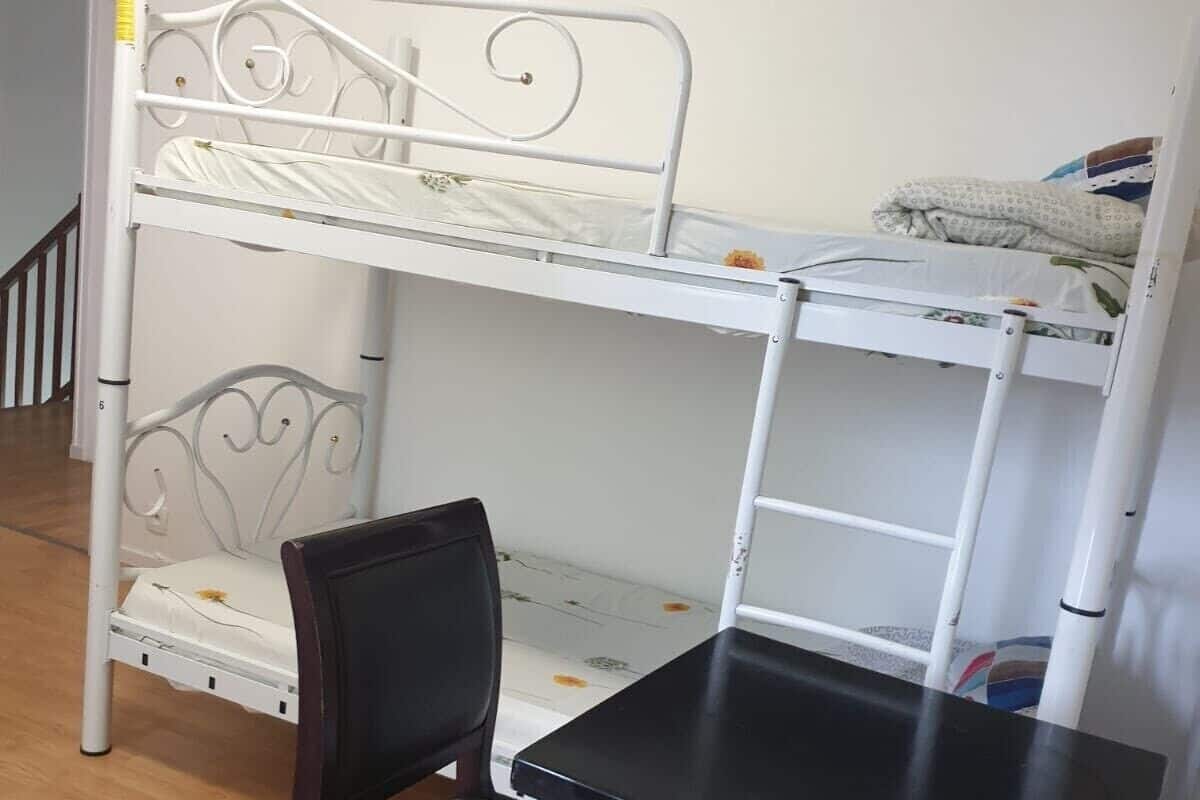 A bunk bed with a black chair and a small table in a room with wooden flooring.