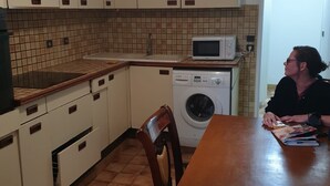 A compact kitchen with a washing machine, a microwave, and a dining table. - Auberge Rose - Hostel (Noisiel)