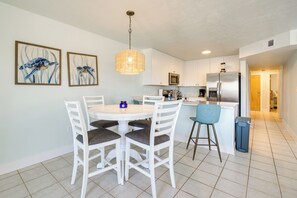 A modern kitchen with white cabinets, a stainless steel refrigerator, and a dining area with a round table and chairs. - Cedar Key Condo w/ Balcony & Gulf Views! (Cedar Key)