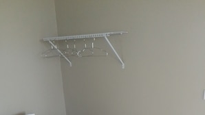 A hotel room with a bed, a white pillow, a brown pillow, and a metal drying rack on the wall. - Two Bedroom Apartment Rental (Paix Bouche)