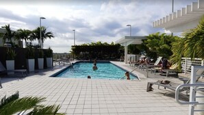 A pool area with tiled flooring, lounge chairs, and palm trees. - Midblock Miami (Miami)
