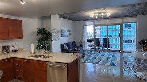 A modern kitchen with a built-in dishwasher, a dining area with a glass table and chairs, and a large sliding glass door leading to a balcony with outdoor seating. - Midblock Miami (Miami)