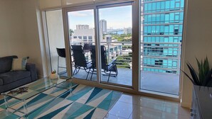 A modern living room with a glass sliding door leading to a balcony, a grey sofa, and a patterned rug. - Midblock Miami (Miami)