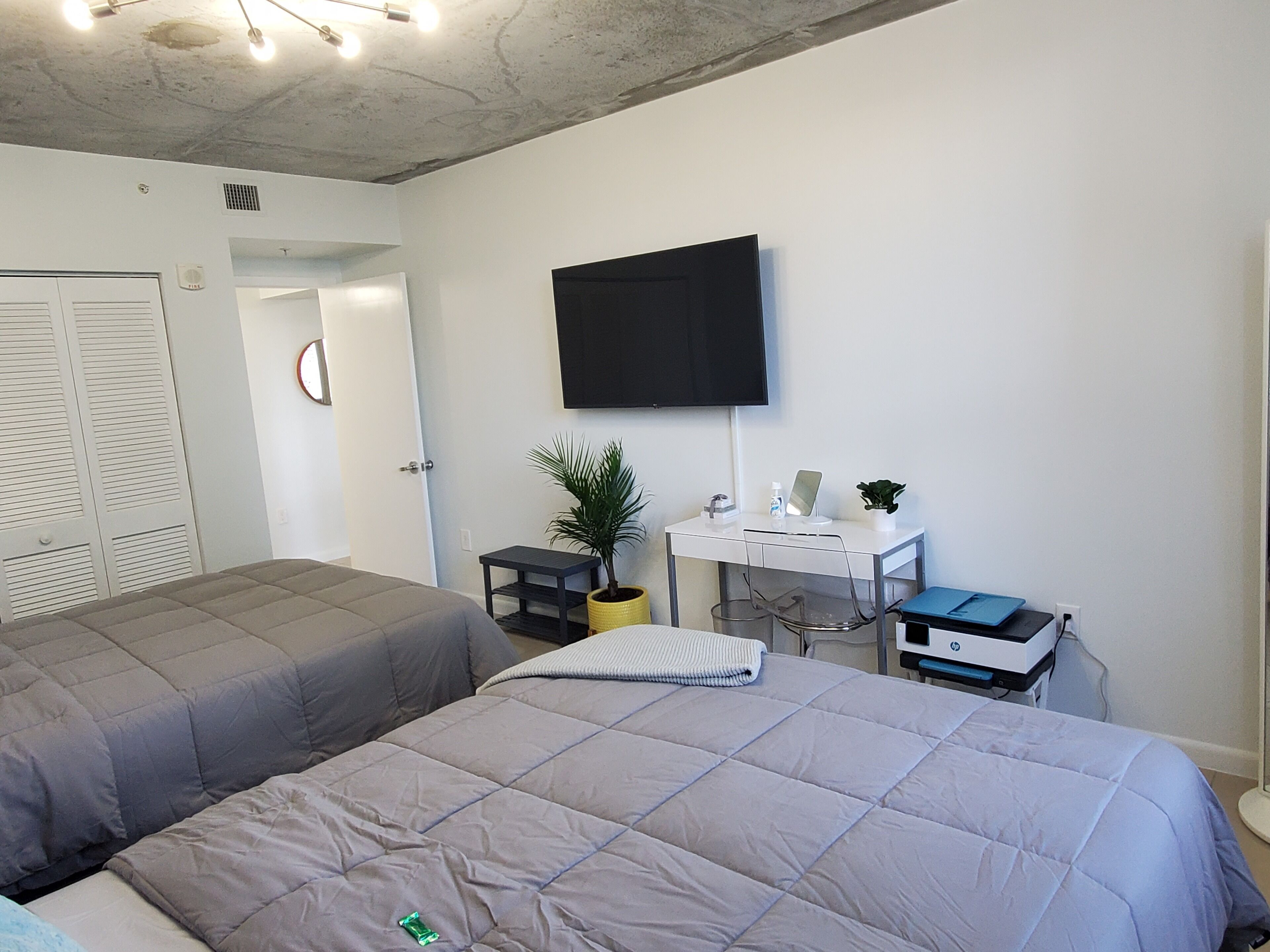 Habitación de hotel con dos camas, un escritorio con computadora, un televisor y una planta en maceta.