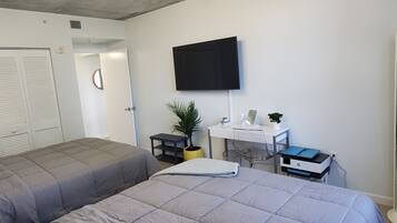 Habitación de hotel con dos camas, un escritorio con computadora, un televisor y una planta en maceta.