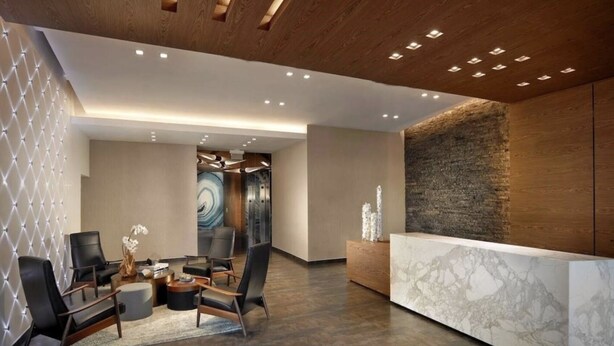 A modern reception area with a marble reception desk, leather chairs, and a wooden ceiling with recessed lighting. - Midblock Miami (Miami)
