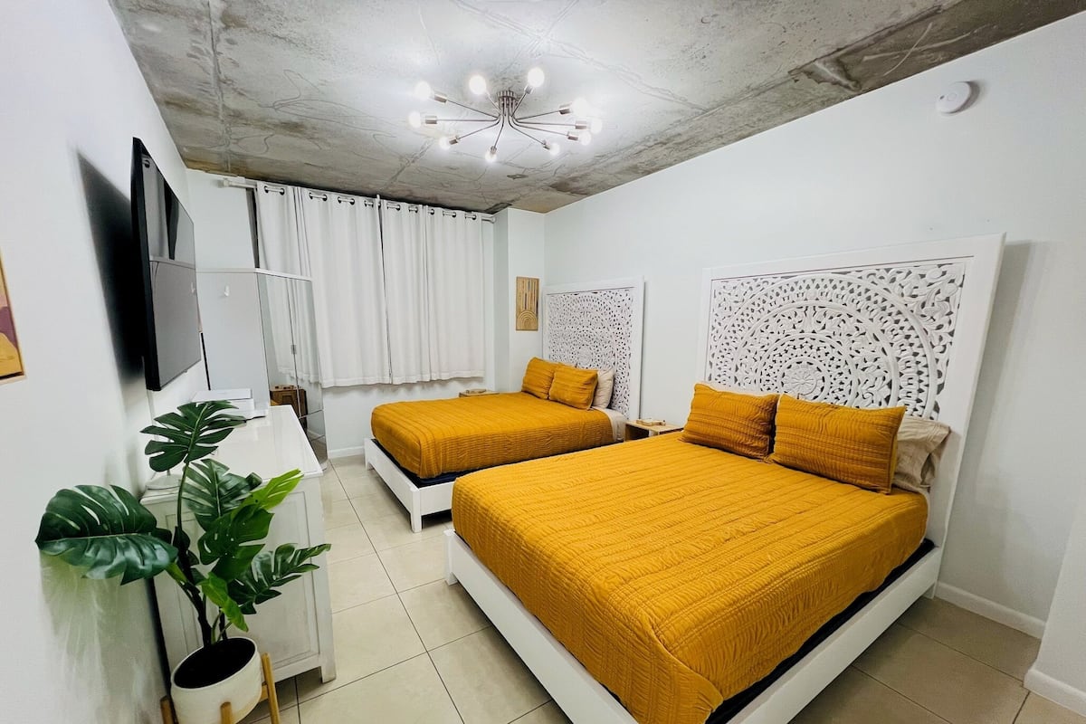 A bedroom with two beds, a TV, a plant, and a ceiling light fixture.