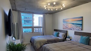 A modern bedroom with two beds, a large window, a painting, and a ceiling light fixture. - Midblock Miami (Miami)