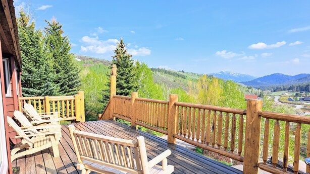A wooden deck with Adirondack chairs, a wooden railing, and a scenic mountain view. - Large mountain home, incredible views, hot tub, game room, minutes from Jackson! (Jackson)