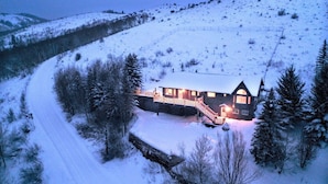 A snow-covered landscape with a house featuring a wooden staircase and a porch. - Large mountain home, incredible views, hot tub, game room, minutes from Jackson! (Jackson)