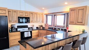 A modern kitchen with wooden cabinets, a black refrigerator, a microwave, a stove, and a large island with bar stools. - Large mountain home, incredible views, hot tub, game room, minutes from Jackson! (Jackson)