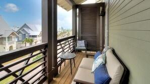Un balcon avec une balustrade en bois, un canapé avec des coussins, une petite table ronde et une chaise.