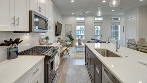 Une cuisine moderne avec des meubles blancs, des appareils en acier inoxydable et des luminaires suspendus.