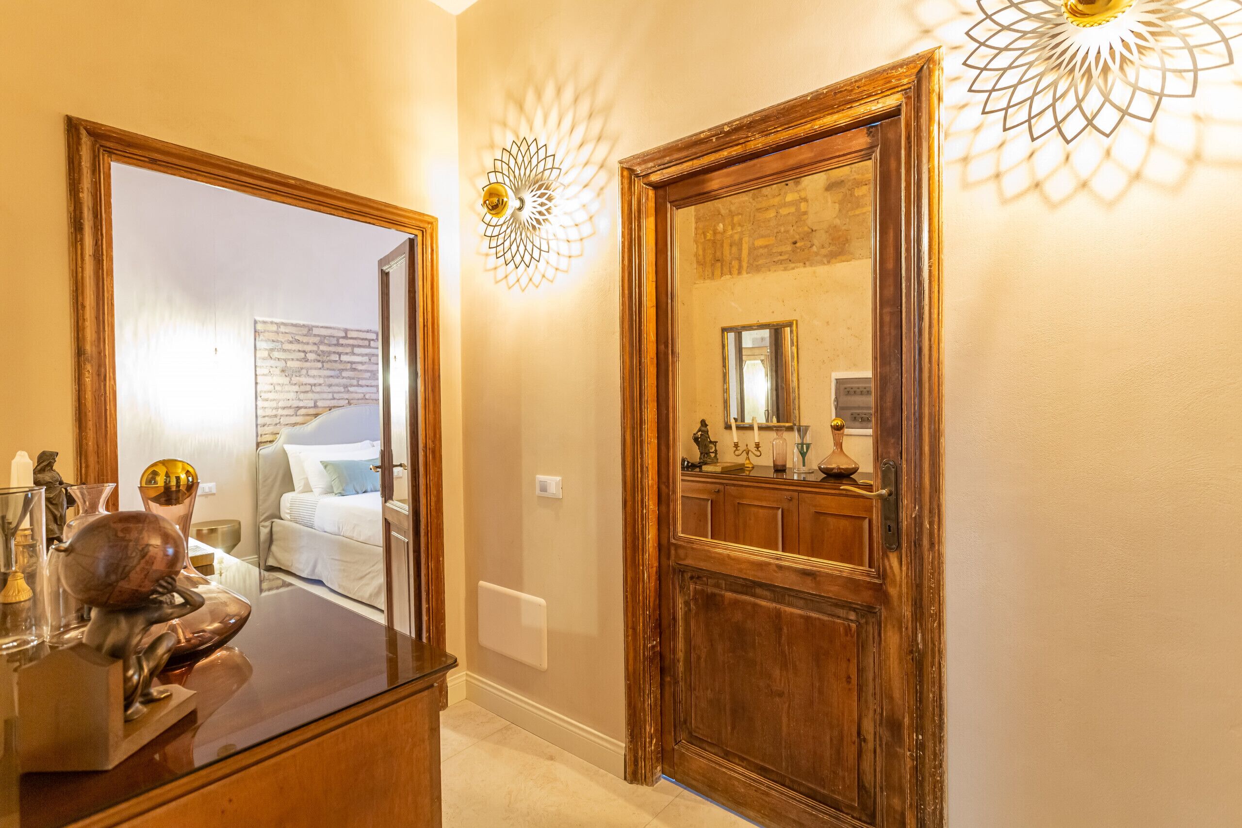 A hallway with a large mirror, a wooden door, and a wall-mounted light fixture.