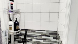 Ein modernes Badezimmer mit weißen, sechseckigen Fliesen, einer Dusche mit schwarzem Duschkopf im Regenstrahl und einem Ablagebereich für Toilettenartikel.