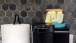 Eine Kaffeemaschine mit Papierhandtuchhalter, einer Rückwand aus sechseckigen Fliesen und vier Bechern Joghurt.