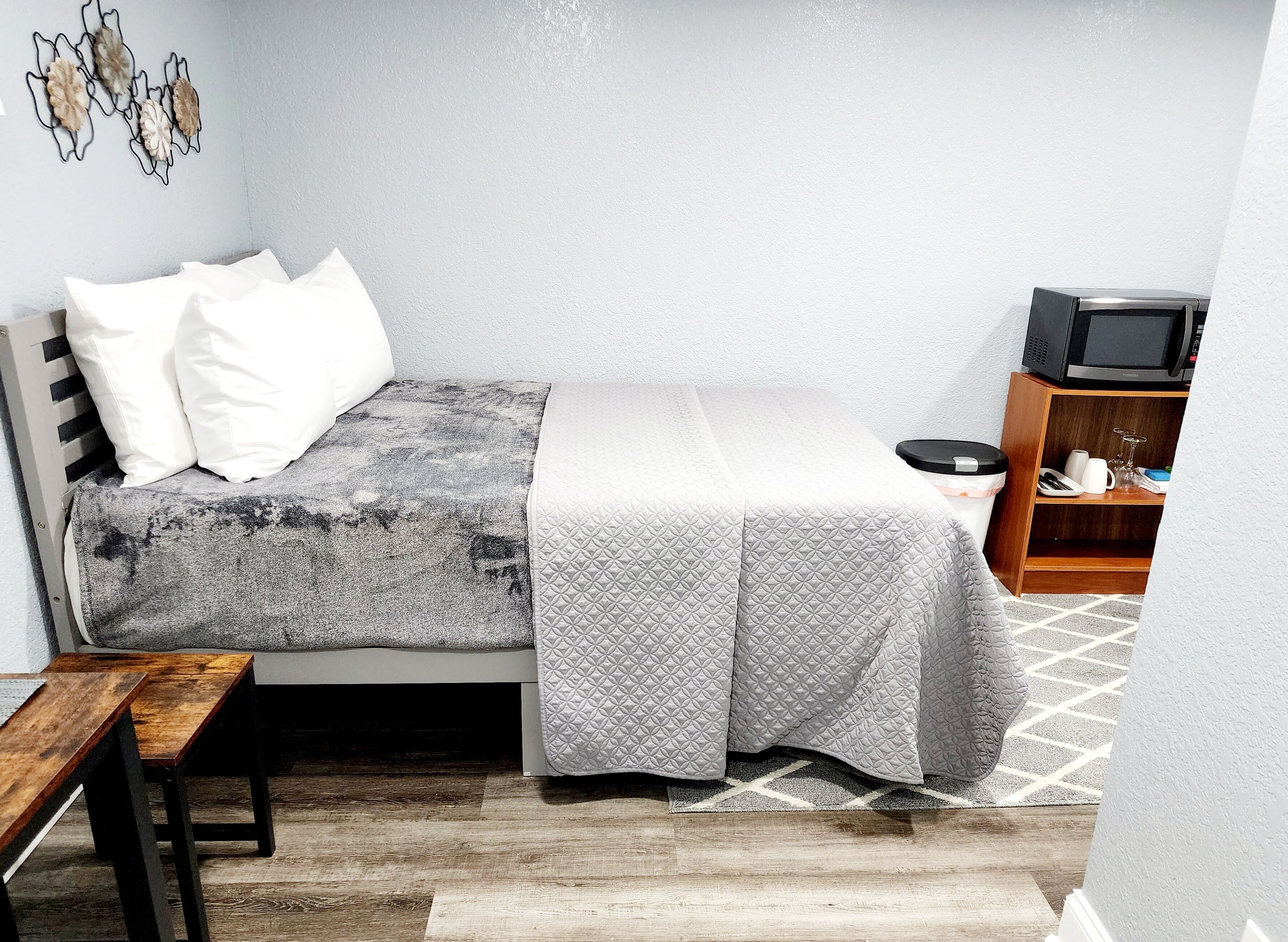 A compact bedroom with a bed, a bedside table, a small wooden cabinet, and a wall-mounted TV.