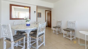 A dining area with a round table, white chairs, and a large mirror. There is a vase with flowers on the table. - Apartamento Tonia by Mallorca North Villas (Port de Pollença)