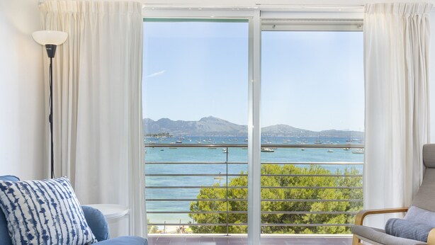 Ein Zimmer mit einer großen Schiebeglasdoor, die auf einen Balkon mit Blick auf das Meer und Boote führt.