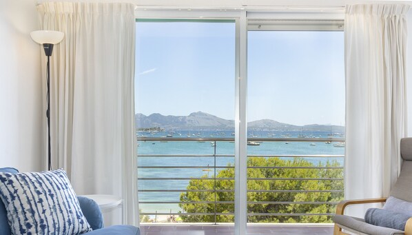 A room with a large sliding glass door leading to a balcony with a view of the sea and boats. - Apartamento Tonia by Mallorca North Villas (Port de Pollença)
