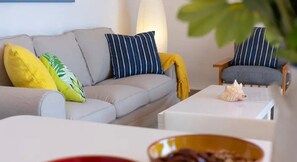 Un salon moderne avec un canapé gris, des coussins à rayures, un plaid jaune et une petite table sur laquelle est posée une coquille décorative.