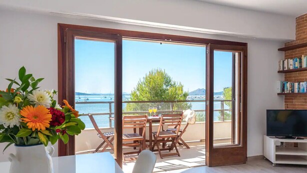 Ein Balkon mit Tisch und Stühlen, einem Fernseher auf einem Schrank und einem Bücherregal.