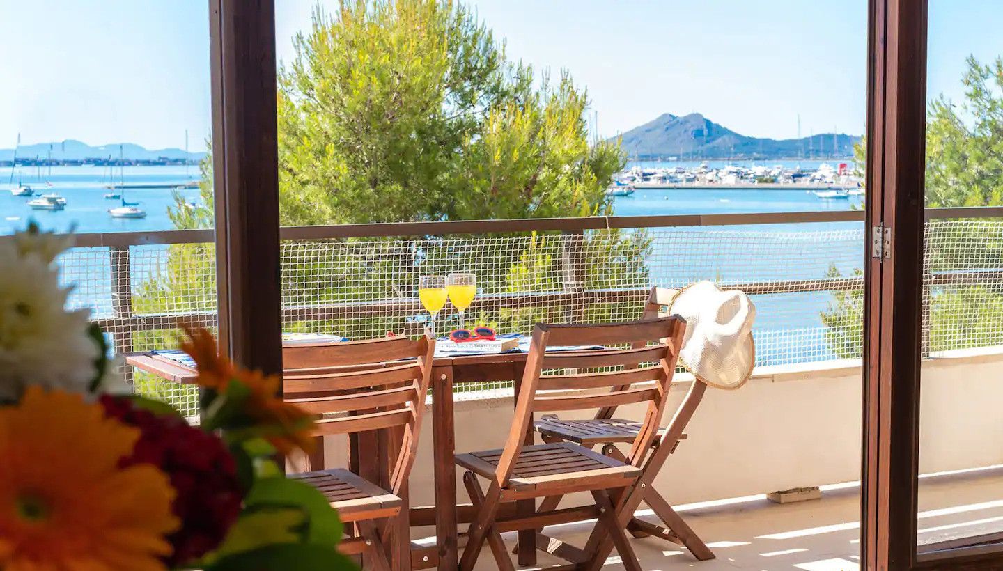 Una mesa y sillas de madera en un balcón con vista al mar y a las embarcaciones.