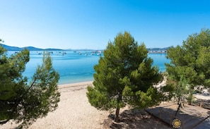A beach with clear blue water, boats, and pine trees.