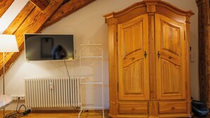 Ein Zimmer mit Holzschrank, Heizkörper, Wand-Fernseher und Kleiderstange.