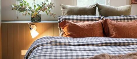 A bedroom with a checkered bedspread, a radiator, and a window with a plant on the sill.